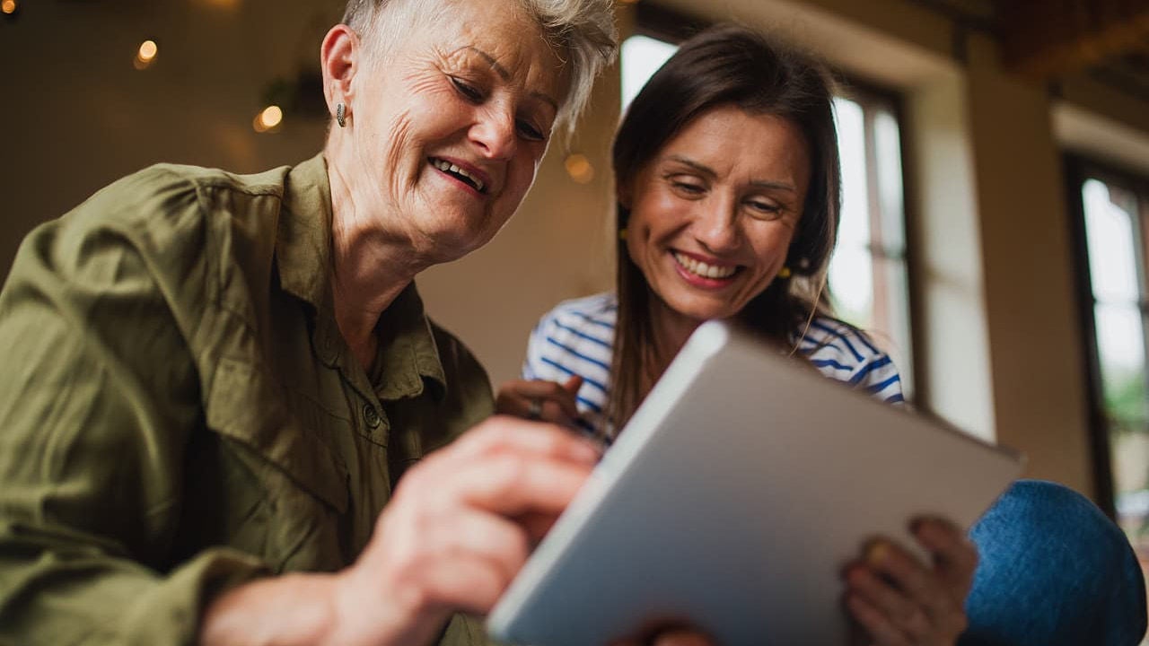 woman helps older woman on tablet