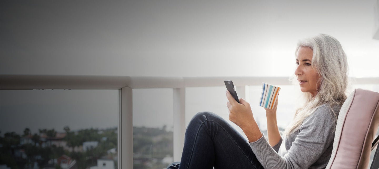 woman relaxing with phone and coffee on balcony